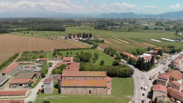 Aerial view of medieval cathedral surrounded by meadows in Tuscany