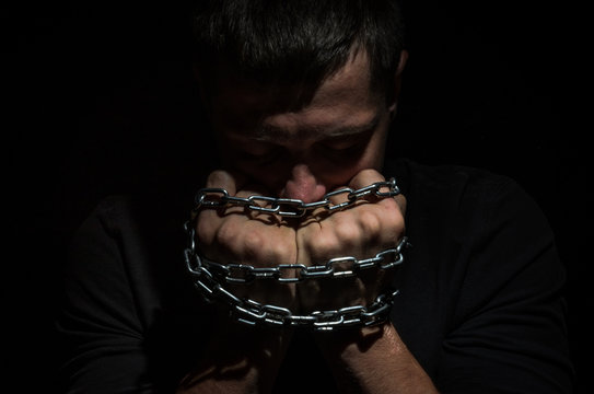Hands bound in metal chains on a black background