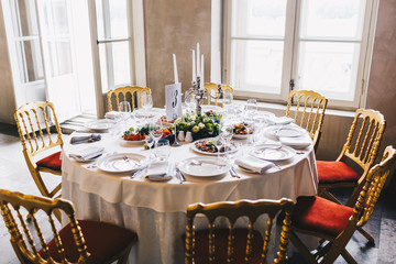 Festive dinner table decorated for many people, tasty dishes, candlestick in middle, white tablecloth, spacious cozy luxury restaurant. Beautiful holiday table. Banquet during wedding. Close up view