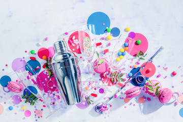 Shaker, straws and cocktail glasses flat lay on a white background with confetti, candies and sweets. Party drink concept with copy space.