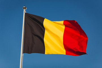Flag of Belgium on mast. National flag against wind blue sky. Flag of Belgium, capital Bruxelless. National symbol of Kingdom of Belgium