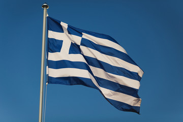 Greek flag with blue and white colours against sky background. Greek banner floats in pure cloudy sky, capital Athens. National landmark concept.