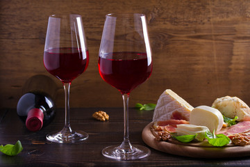 Glasses and bottle of wine with cheese, bread, nuts and jamon or prosciutto on dark wooden background. Wine and food concept