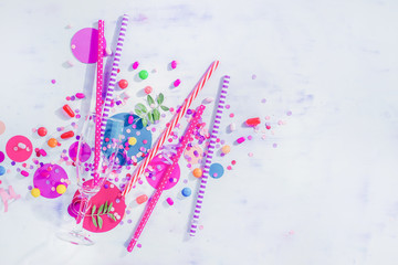 Party concept with bar supplies, colorful flat lay with copy space. Tall cocktail glass with straws, candies, sweets and confetti.