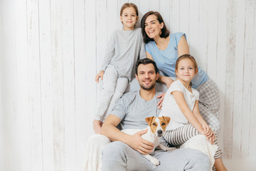 Horizontal shot of friendly family pose together against white background: two little sisters,...