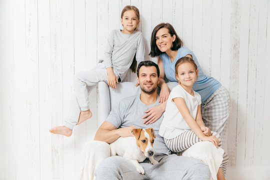 Friendly family of four memebers: cheerful European brunette female, her husband, two daughters and favourite pet, have good relationships, support each other. Affectionate parents with children