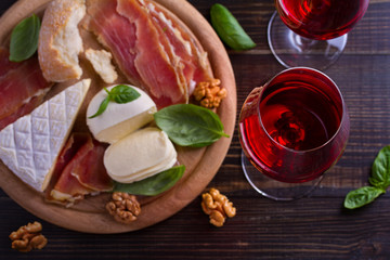 Glasses of wine with cheese, bread, nuts and jamon or prosciutto on dark wooden background. Wine and food concept. View from above, top studio shot