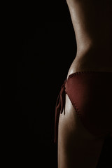 Half view (left) of a topless Asian sexy woman in red lingerie, isolated over black background.