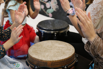 Fototapeta na wymiar Kids play jembe drum in a montessori music therapy classroom with parents, hands close up