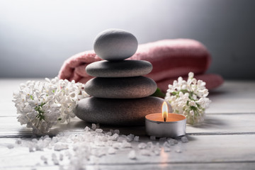 Fototapeta na wymiar Spa still life with pyramid of zen stones,burning candle, sea salt, towel and white flowers on white wooden table