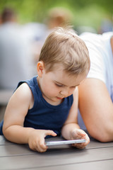 little boy sits next to dad and is highly concentrated with a cell phone in his hands 