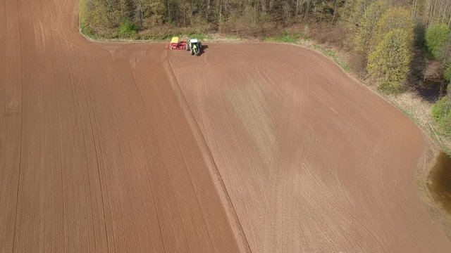 Farm tractor sowing wheat on spring farm field, aerial view