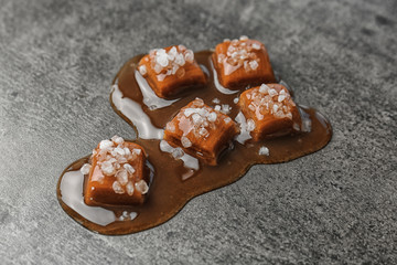 Delicious candies with caramel sauce and salt on gray background