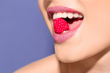 Beautiful young model with creative makeup holding candy in lips on color background