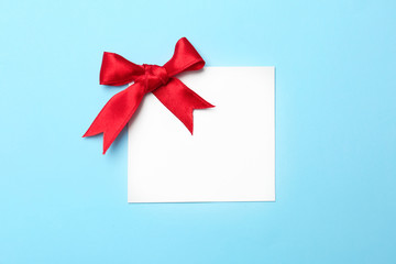 Blank gift tag with satin ribbon on color background, top view