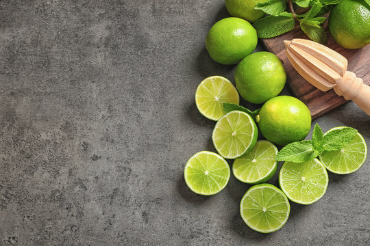 Flat lay composition with ripe limes, mint and juicer on grey background. Refreshing beverage recipe