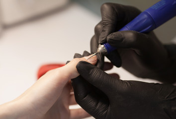 Manicure in process.Closeup shot of a woman in a nail salon receiving a manicure by a beautician with nail file. Woman getting nail manicure. Beautician file nails to a customer.