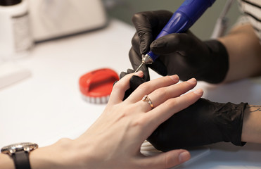 Manicure in process.Closeup shot of a woman in a nail salon receiving a manicure by a beautician with nail file. Woman getting nail manicure. Beautician file nails to a customer.