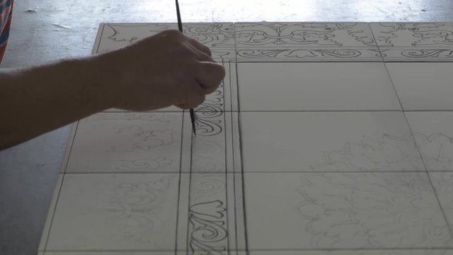 Male hand tracing paint desing on white ceramic tiles