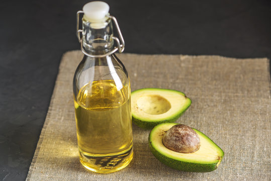 Avocado fruit and oil in glass bottle on dark background. Concept organic eco products for food and cosmetic procedures