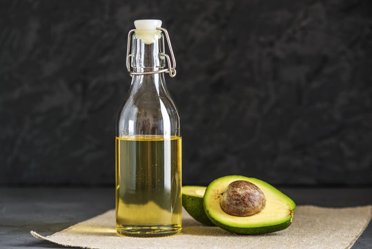 Avocado fruit and oil in glass bottle on dark background. Concept organic eco products for food and cosmetic procedures