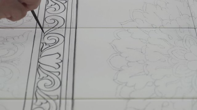 Male hand tracing paint desing on white pottery tiles