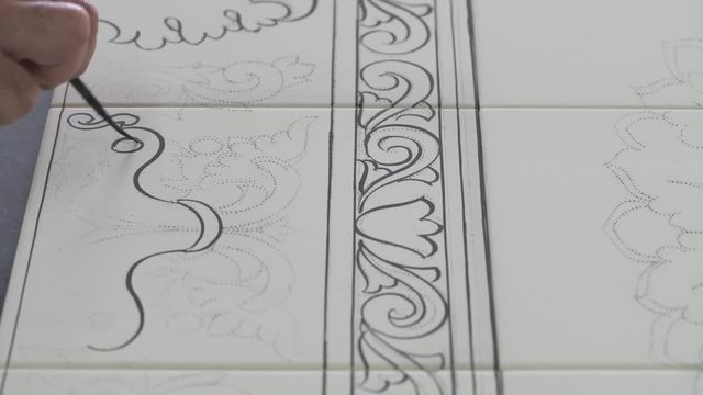 Male hand tracing paint desing on white pottery tiles