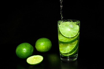 Cold detox water with ice and fresh ripe slice green limes on black background.