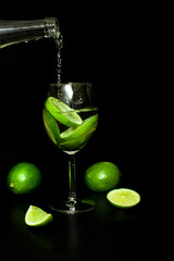 wineglass of cold drink with ice and fresh ripe slice green limes on black background.