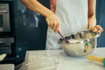 Asian women are mixing the ingredients of a cake in a stainless bowl in her kitchen for weekend party.