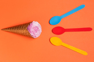 a horn with ice cream or with cream horizontally on an orange background, near three different-colored spoons, the concept of a summer