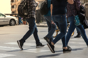 People stranded and distracted crossing the street in the pedestrian crossing at a busy intersection crowded and crowded in the midst of traffic only showing up the legs and feet. Walking and talking 