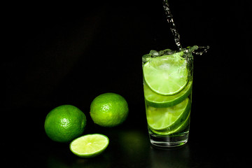 drink with ice and fresh ripe green limes on black background