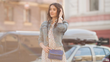 Young beautiful stylish girl walking and posing in short summer dress in city. Outdoor summer portrait of young woman