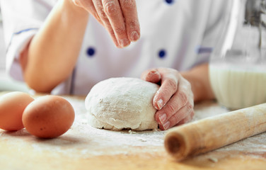 Close up of female chef powdering flour on dough. Professional baker preparing bread. 
