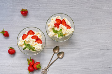 Dessert with sliced strawberries and cream cheese in the glass bowls on a gray background with copy space. Decorated with vintage spoons and fresh mint leaves. Traditional summer snack. Top view