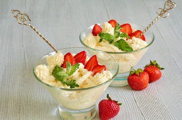 Cold summer dessert with sliced strawberries, cheese cream in the glass bowls on the gray kitchen table decorated with fresh mint leaves and two vintage spoons. Close up view