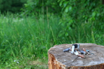 Spent batteries, coated with corrosion. Different shapes and sizes. lie on the edge of a wooden stump. Environmental protection, recycling.