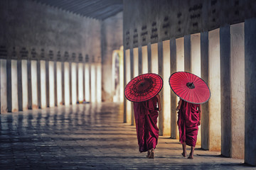 Two buddhist monk novice holding red umbrellas and walking in pagoda, Myanmar.