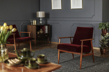 Real photo of a wine red armchair standing in the middle of an elegant, dark living room interior...