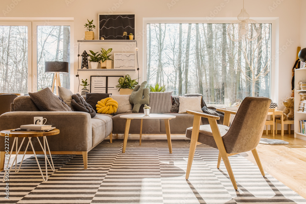 Wall mural low angle view of a scandinavian, sunlit living room interior with a gray armchair and sofa, and a b