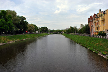 City landscape, river embankment, green trees from one side and colorful houses on another, cloudy spring day, Kharkiv, Ukraine