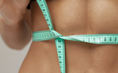 hands measuring waist with a tape. Fit and healthy woman on grey background