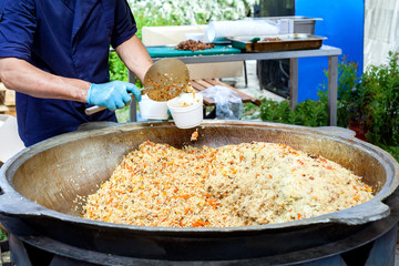 Seller is putting pilaf into a cardboard plate at the street food festival