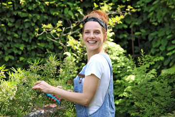 Hübsche rothaarige Frau schneidet lachend Gartenpflanzen