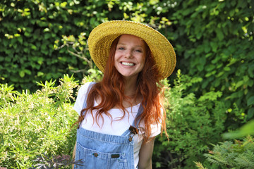 Hübsche rothaarige Frau mit einem gelben Strohhut steht in einem Garten und lacht