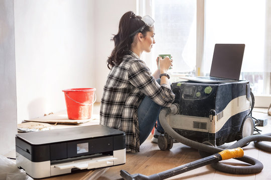 Young woman renovating her new flat, drinking coffee, looking at laptop