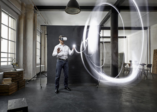 Mature man with vr glasses light painting in front of black backdrop in loft