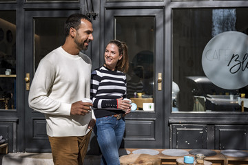Man and woman with takeaway cups walking outside a cafe