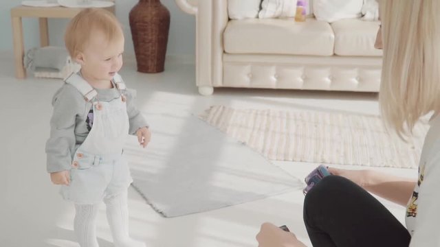 Little lovely girl takes her shoes. Happy beautiful baby gives her shoes to her mom. Slow motion
